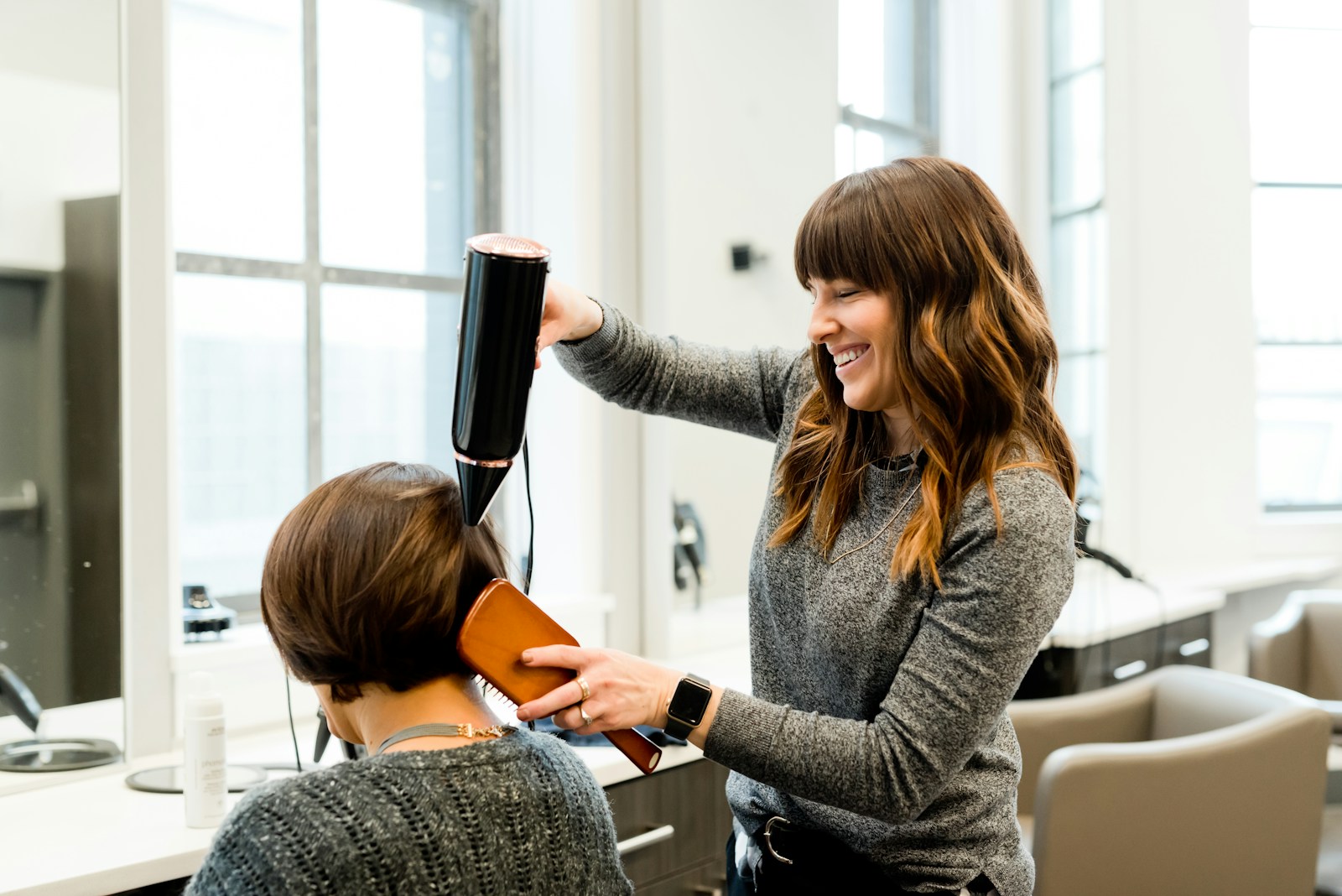Cabeleireira cuidando do cabelo de uma cliente em um salão iluminado